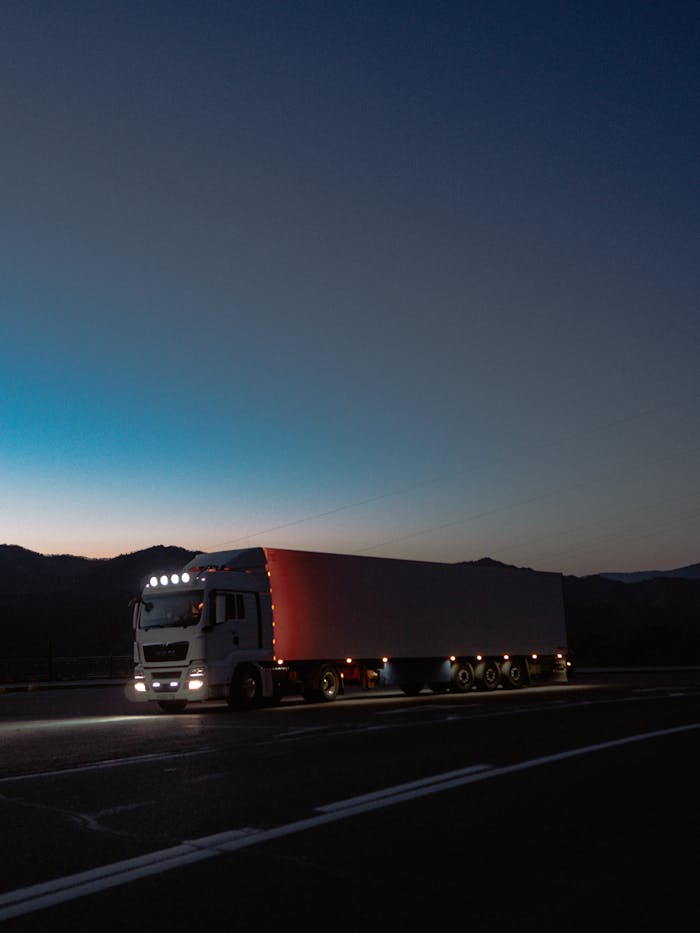 A large truck travels on a highway at dusk surrounded by mountains, showcasing travel and logistics.